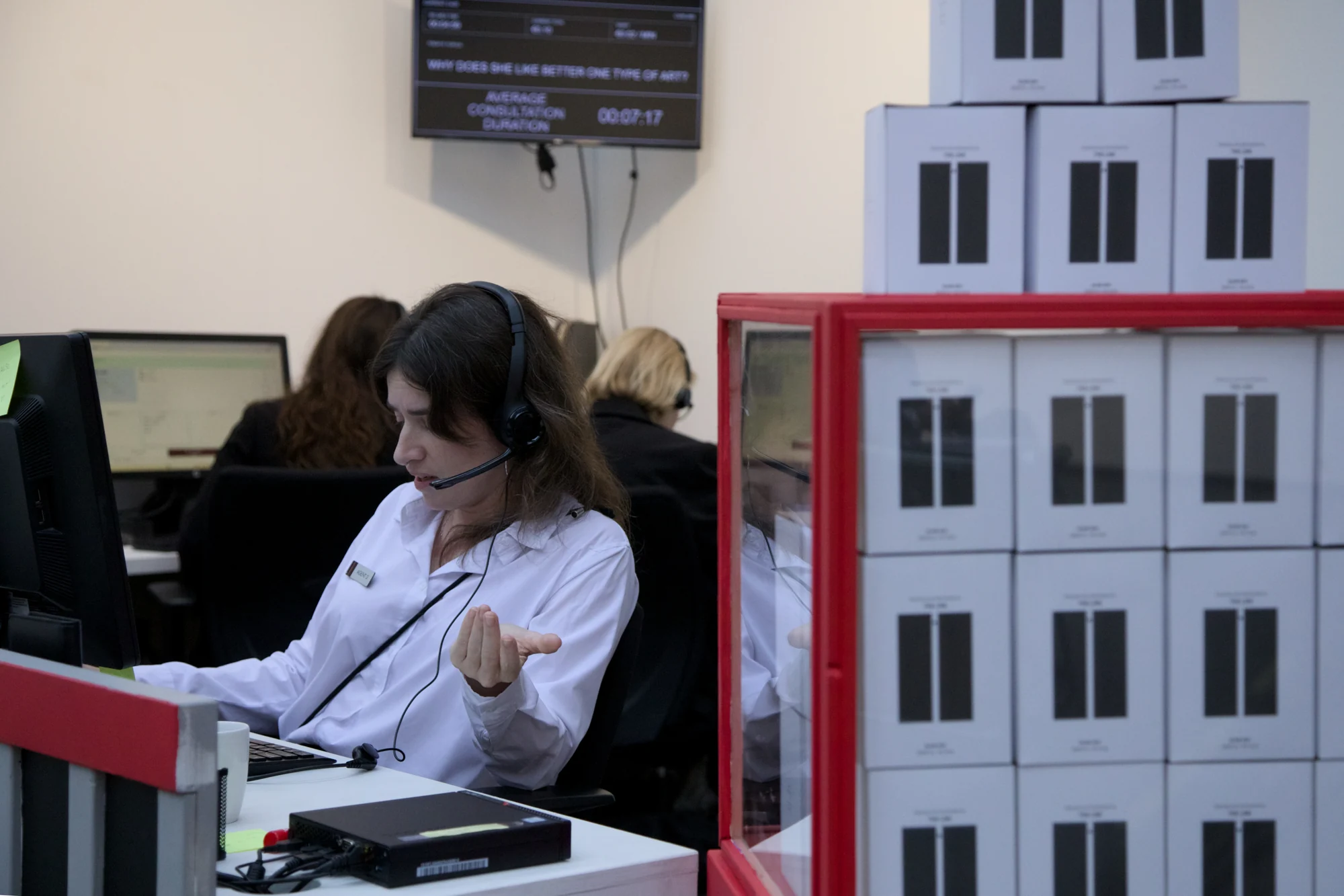 An agent on a headset beside a red display cabinet stacked with Blind Boxes.